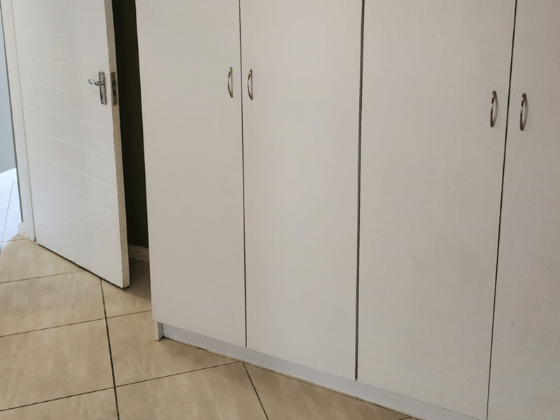 A bedroom interior featuring built-in white cupboards and neutral tiled flooring, providing a clean and functional storage space.