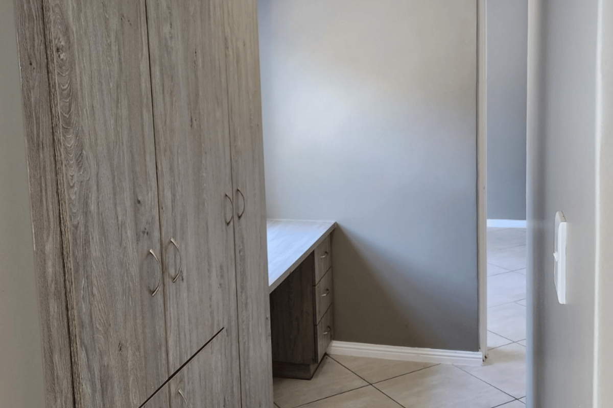A clean bedroom featuring modern wood-look built-in cupboards and a matching integrated desk, finished with neutral tiled flooring.
