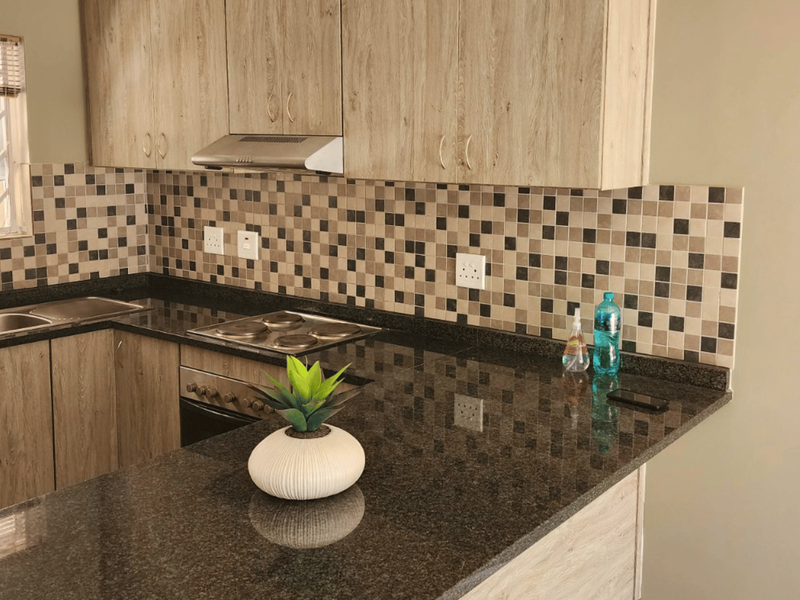Modern kitchen featuring wood-look laminate cabinetry, dark granite countertops, a mosaic tile backsplash, and integrated stainless steel appliances.