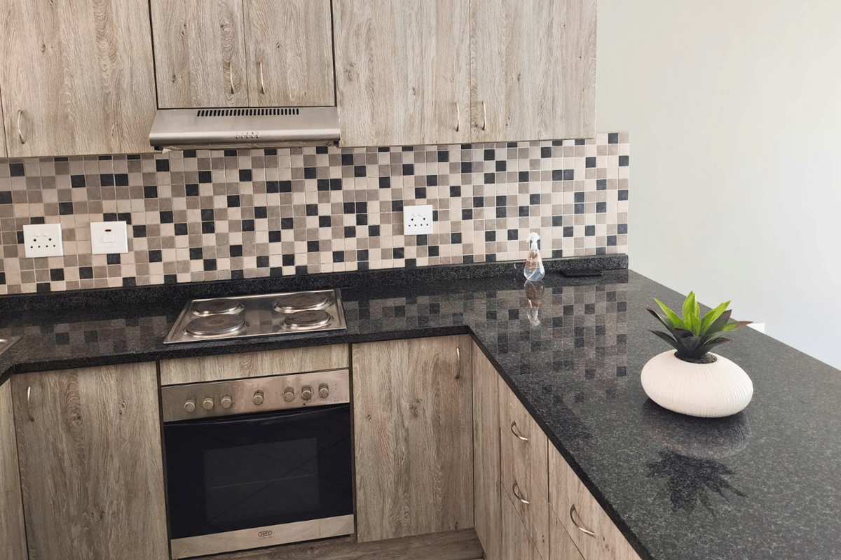 Modern kitchen featuring wood-look laminate cabinetry, dark granite countertops, a mosaic tile backsplash, and integrated stainless steel appliances.