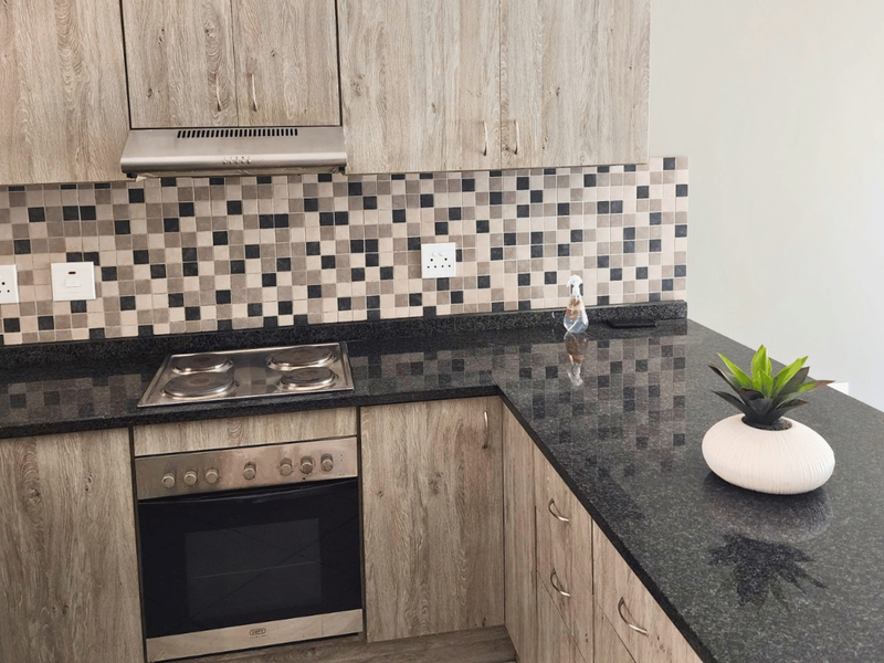 Modern kitchen featuring wood-look laminate cabinetry, dark granite countertops, a mosaic tile backsplash, and integrated stainless steel appliances.