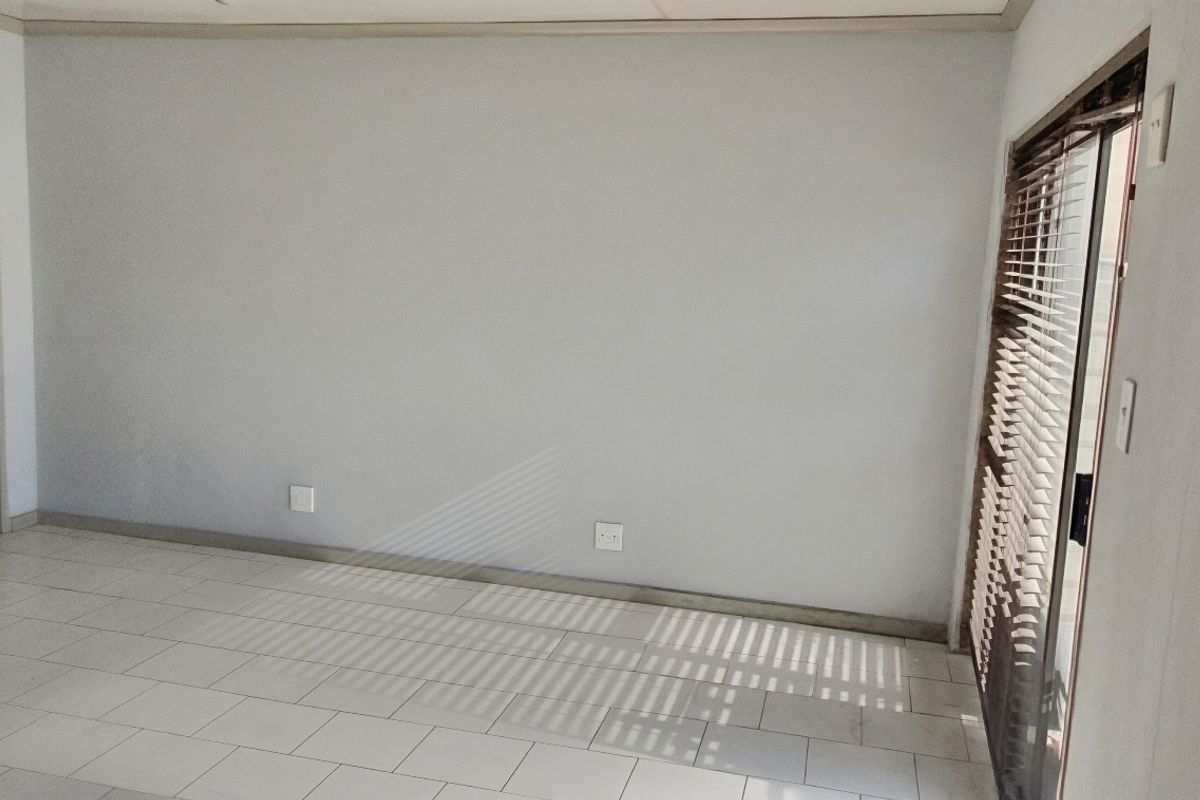 An empty living room featuring neutral tiled flooring, clean walls, and a sliding glass door providing natural light.