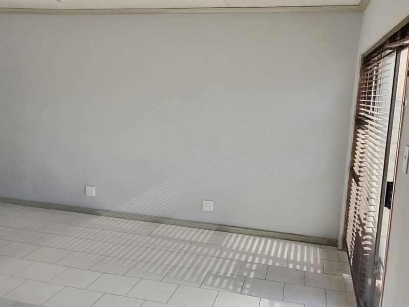 An empty living room featuring neutral tiled flooring, clean walls, and a sliding glass door providing natural light.