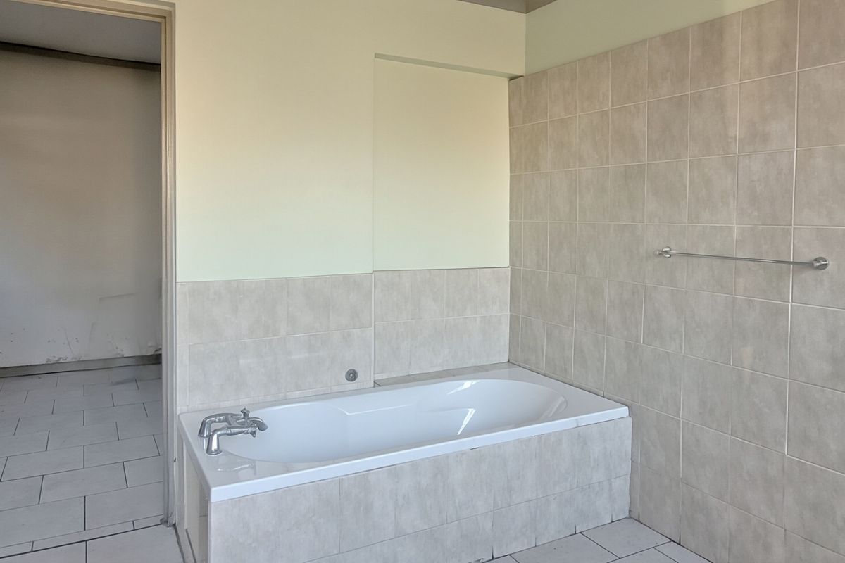 A functional bathroom featuring a built-in bathtub with tiled surround and wall tiling, presenting a clean, neutral space ready for personalization.