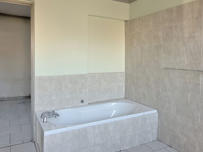 A functional bathroom featuring a built-in bathtub with tiled surround and wall tiling, presenting a clean, neutral space ready for personalization.