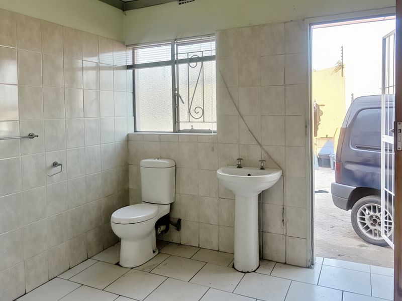 A functional bathroom featuring a pedestal basin and toilet, with full-height wall tiling and direct access to the exterior.