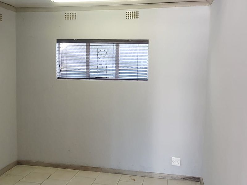 An empty bedroom featuring tiled flooring, horizontal window blinds, and ceiling ventilation vents, presenting a blank canvas for potential renovation or interior design updates.