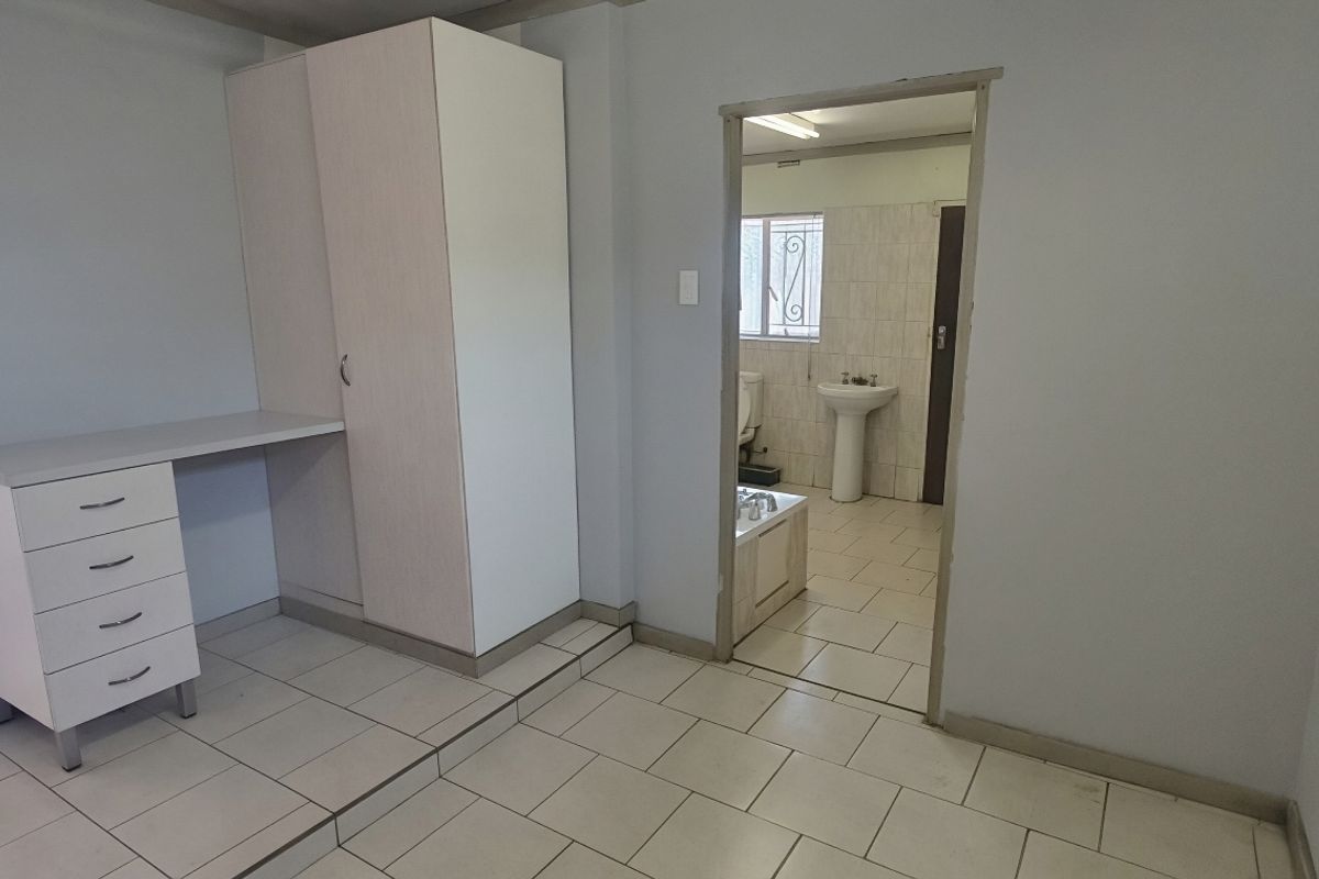 A bedroom featuring tiled flooring, a built-in wardrobe with an integrated desk, and direct access to an en-suite bathroom.