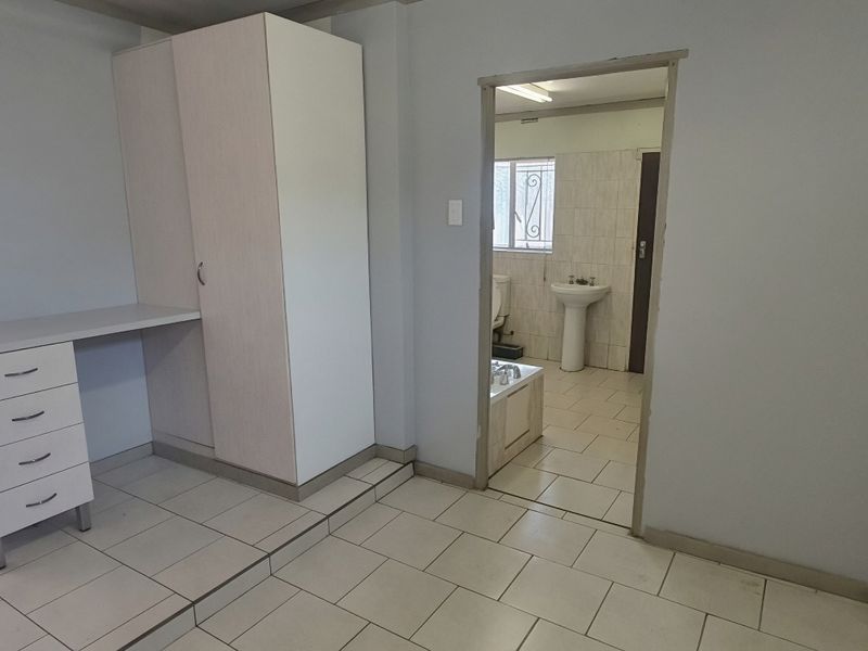 A bedroom featuring tiled flooring, a built-in wardrobe with an integrated desk, and direct access to an en-suite bathroom.