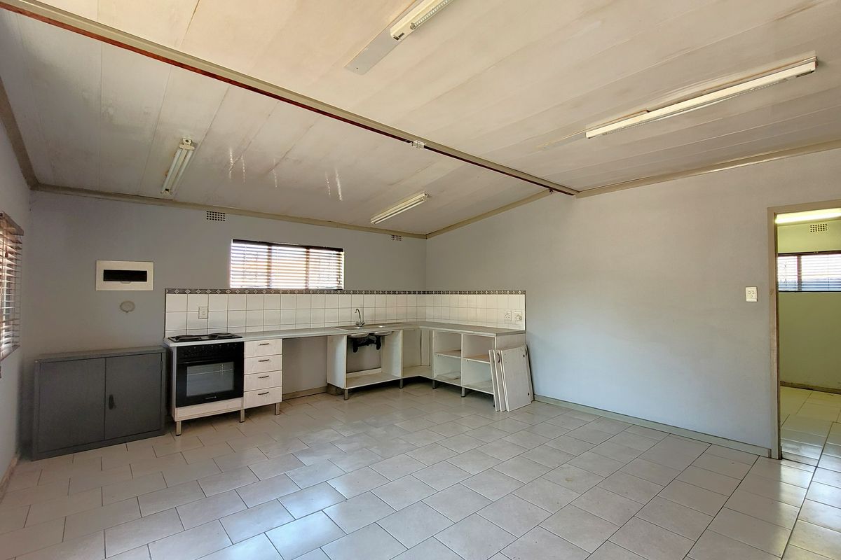 An empty, dated kitchen featuring tiled flooring, a built-in oven, and basic cabinetry with some missing doors, offering potential for renovation.