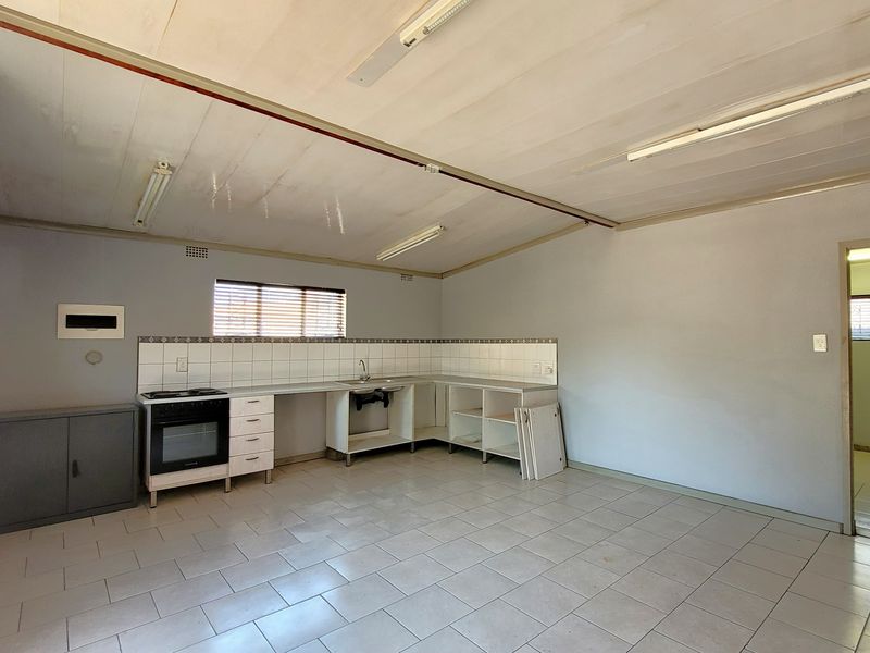 An empty, dated kitchen featuring tiled flooring, a built-in oven, and basic cabinetry with some missing doors, offering potential for renovation.