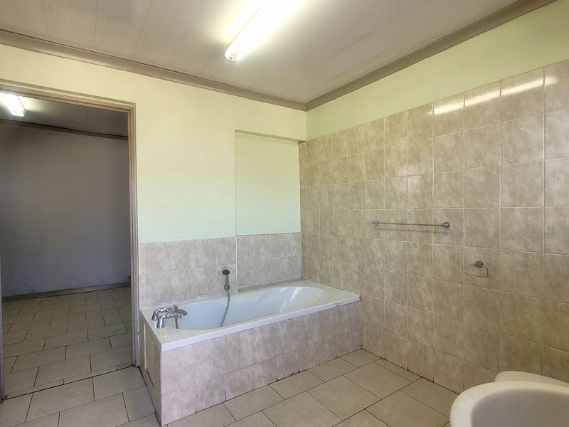A functional bathroom featuring a built-in bathtub with tiled surround, neutral wall finishes, and tiled flooring, offering a clean and simple layout.