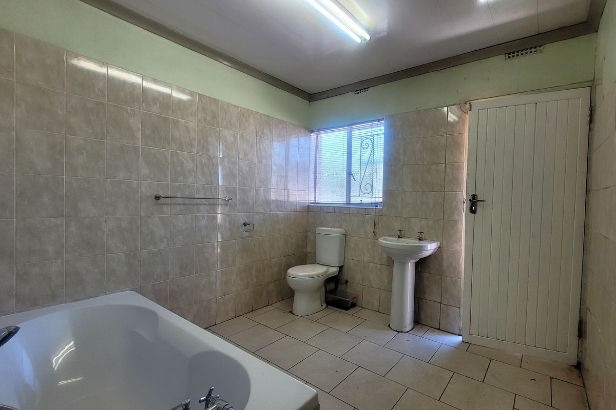 A dated bathroom featuring a bathtub, pedestal basin, and toilet, finished with neutral ceramic wall and floor tiles.