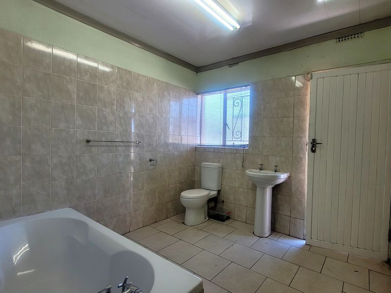 A dated bathroom featuring a bathtub, pedestal basin, and toilet, finished with neutral ceramic wall and floor tiles.