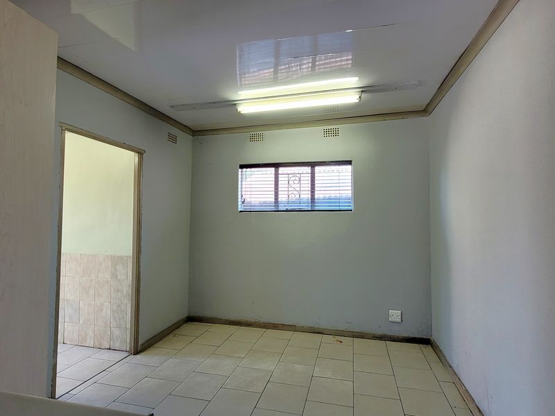 An empty bedroom featuring tiled flooring, a window with security bars, and basic fluorescent lighting, offering a blank canvas for renovation.