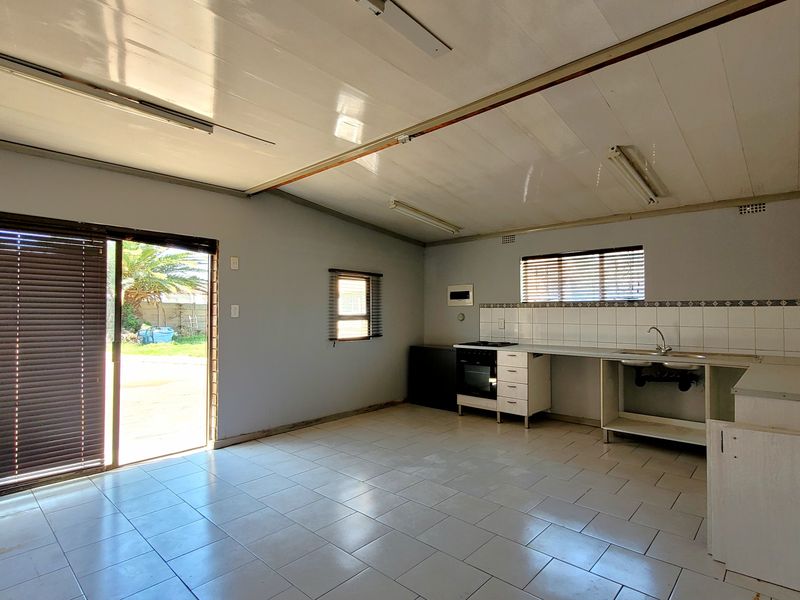 Open-plan kitchen and living area featuring tiled floors, built-in cabinetry with oven and hob, and direct access to the garden through a sliding door.