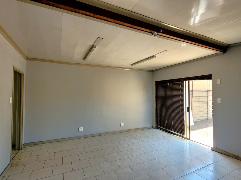 An empty living room featuring tiled flooring, an exposed ceiling beam, and a sliding glass door providing access to the exterior.