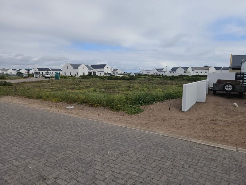 A vacant residential plot featuring a paved driveway and a partial boundary wall, situated within a developed estate.