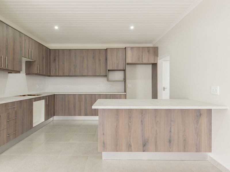 Modern kitchen featuring wood-look laminate cabinetry, stone countertops, a central island, and neutral tiled flooring in a clean, well-lit open space.