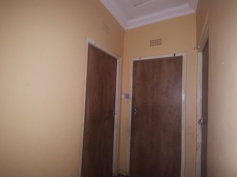A functional interior hallway featuring neutral wall finishes, multiple wooden doors, and integrated security alarm system components.