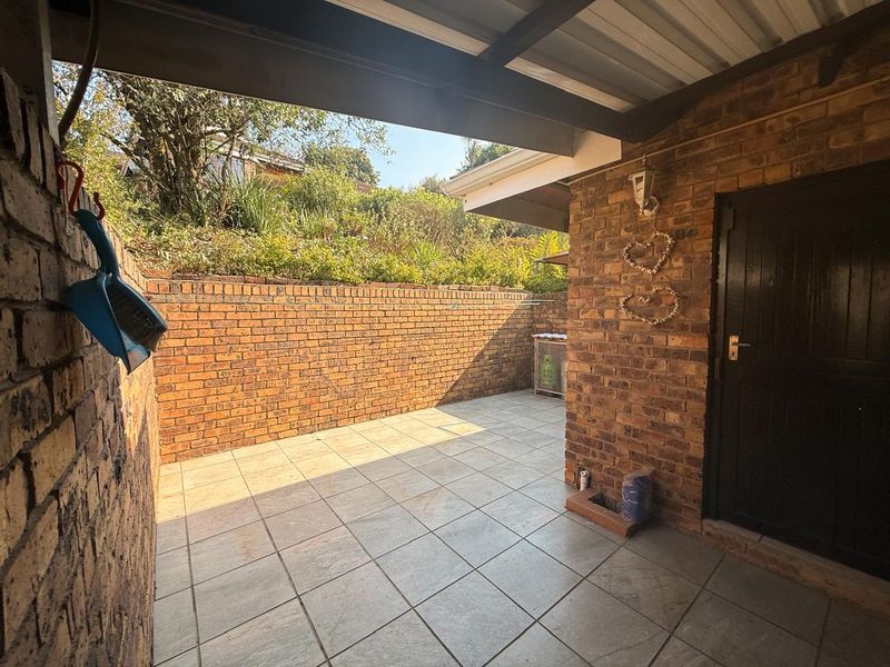 A covered outdoor patio area featuring face-brick walls and tiled flooring, providing a functional space for outdoor living.