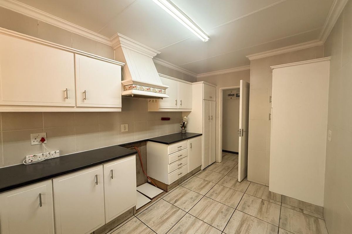 A functional kitchen featuring white cabinetry, dark countertops, tiled flooring, and a dedicated space for a stove, presenting a clean, blank canvas for updates.
