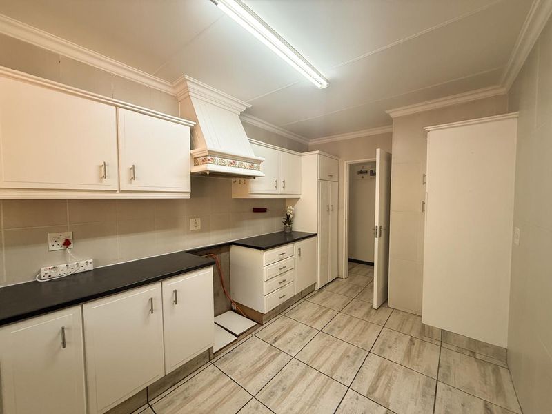 A functional kitchen featuring white cabinetry, dark countertops, tiled flooring, and a dedicated space for a stove, presenting a clean, blank canvas for updates.
