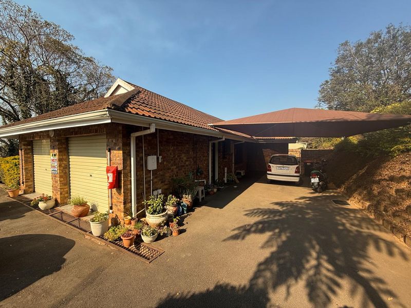 Front exterior view of a brick townhouse featuring a double garage, a covered carport, and a paved driveway area.