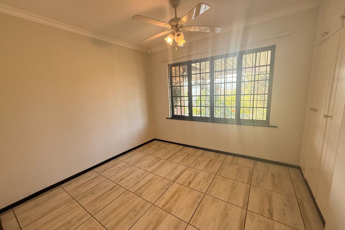 A bright, empty bedroom featuring tiled flooring, built-in cupboards, and a ceiling fan, offering a clean canvas for personalization.
