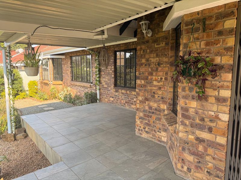 A covered patio area featuring tiled flooring and exposed brick walls, providing a functional outdoor space adjacent to the main building structure.