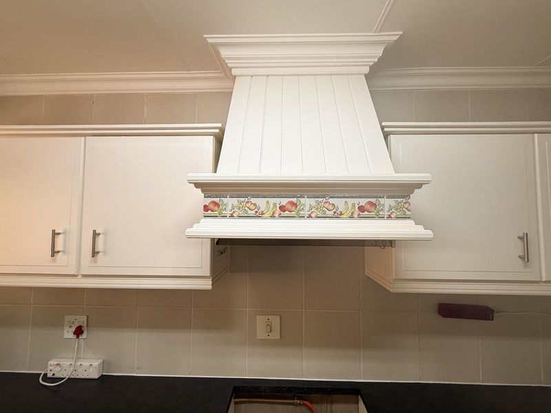A kitchen area featuring white cabinetry, a decorative tiled extractor hood, and a neutral tiled backsplash.