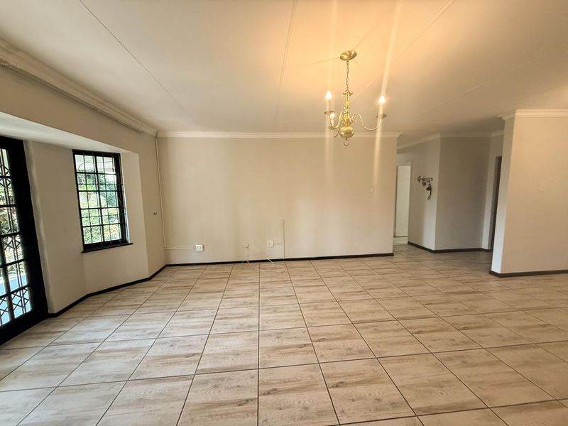 A spacious, empty living area featuring light wood-look floor tiles, a classic chandelier, and access to the outdoors through black-framed french doors.