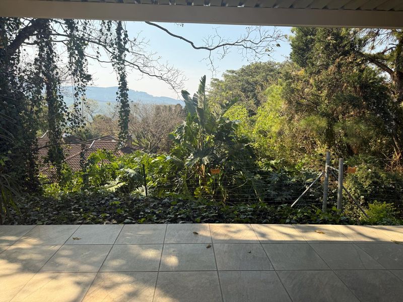 A covered patio area featuring tiled flooring and an elevated view overlooking the lush garden and surrounding landscape.