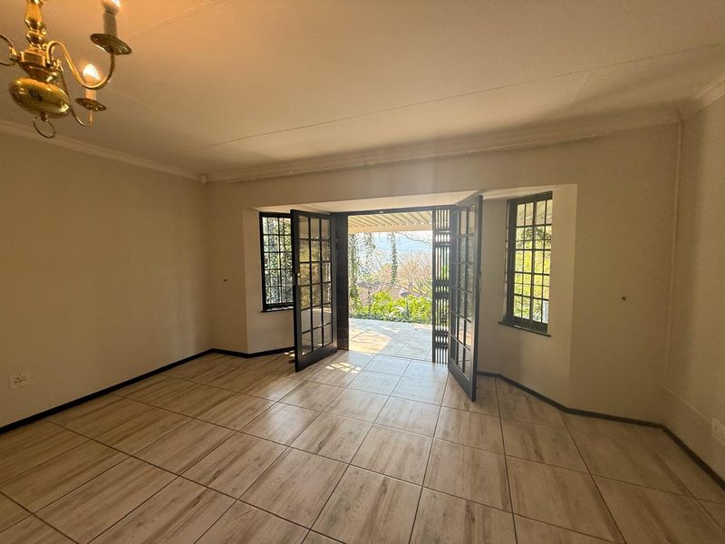 An empty living room featuring tiled flooring, coving, and french doors opening onto an outdoor patio area with garden views.