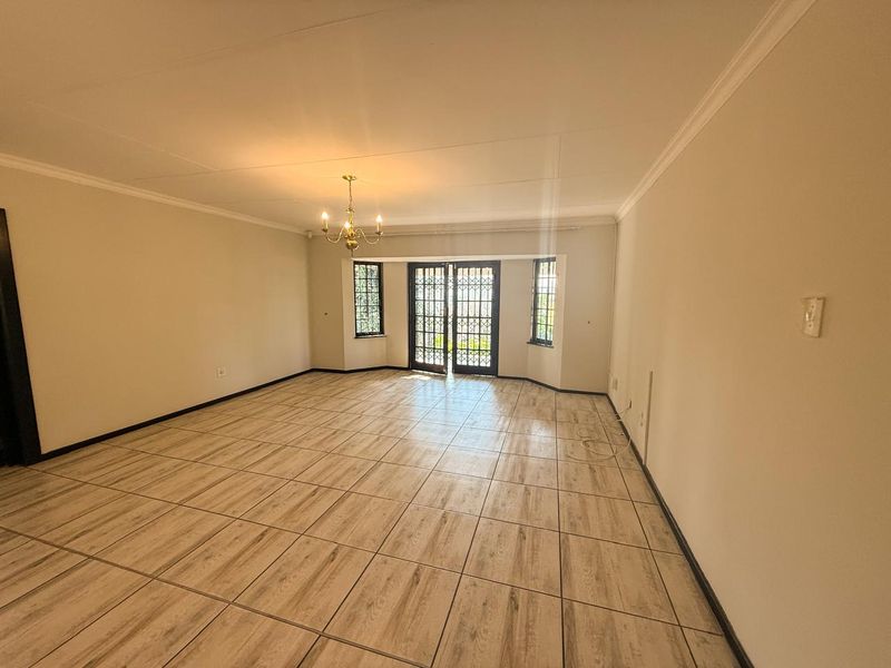 Spacious, empty living room featuring wood-look tiled flooring, decorative coving, and secure french doors leading to the exterior.