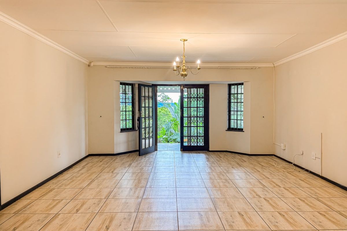 Spacious, empty living room featuring wood-look tiled flooring, classic coving, and double french doors opening to a garden view.