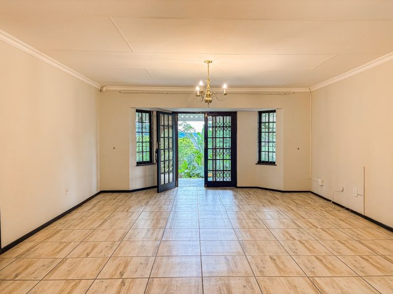 Spacious, empty living room featuring wood-look tiled flooring, classic coving, and double french doors opening to a garden view.