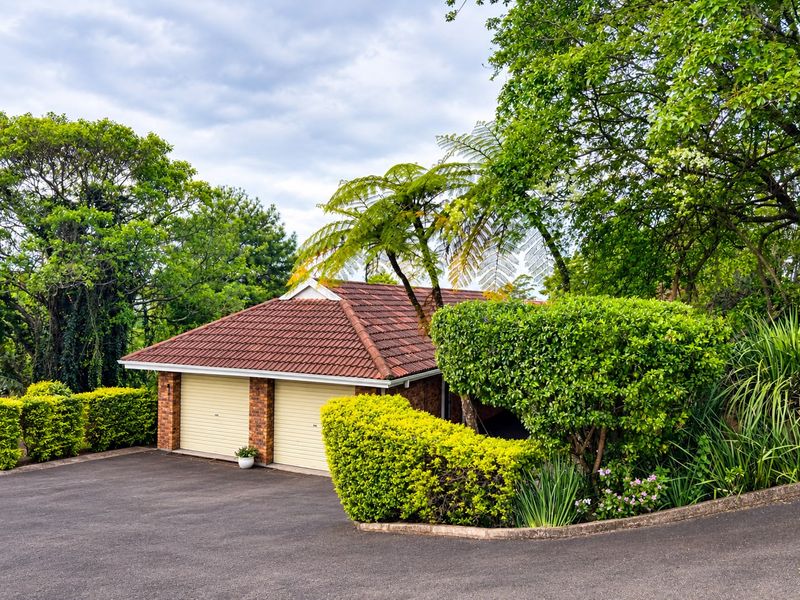 A well-maintained double garage with a tiled roof and brick detailing, situated at the end of a paved driveway surrounded by established garden landscaping.