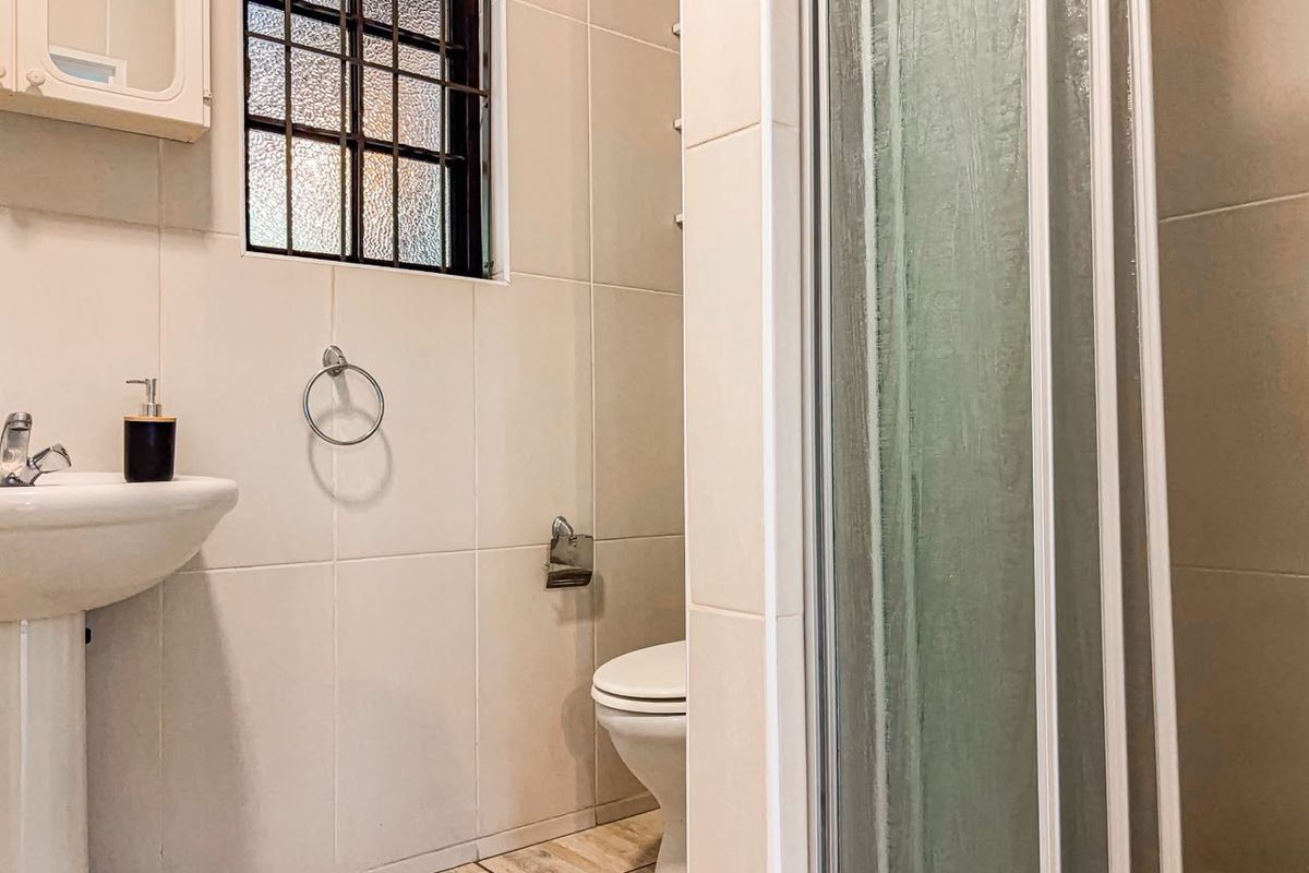 A functional bathroom featuring a pedestal basin, toilet, and a shower enclosure with tiled finishes and an obscured glass window.