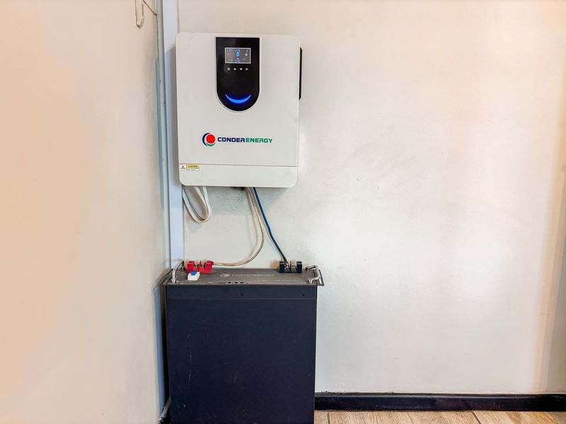 Wall-mounted solar inverter and floor-standing lithium battery storage unit installed in a utility area.