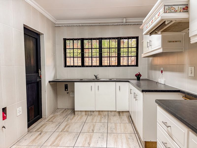 A functional kitchen featuring white cabinetry, dark countertops, tiled walls and flooring, and a window with security bars.
