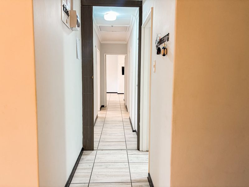 A clean, tiled hallway connecting multiple rooms, featuring a folding door and an accessible electrical distribution board.