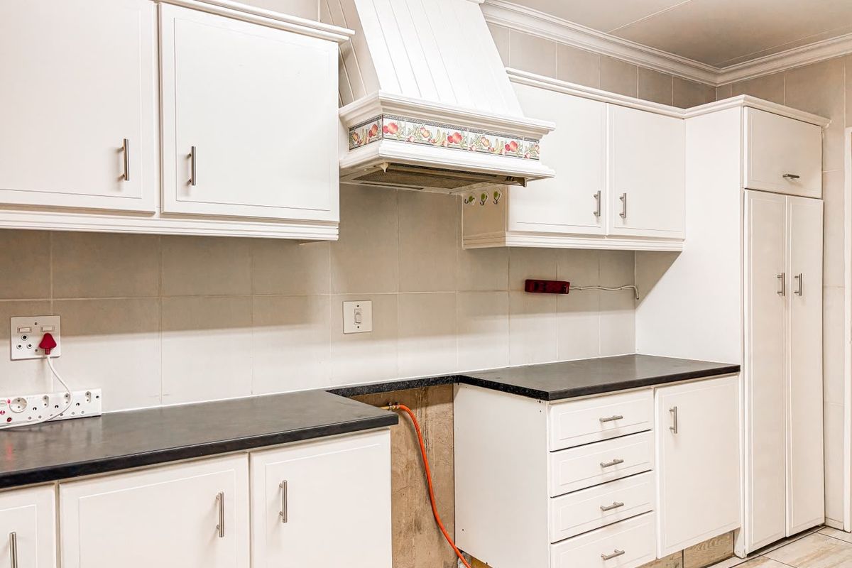 A kitchen featuring white cabinetry, tiled backsplash, and dark countertops, currently missing a stove unit with exposed gas piping.