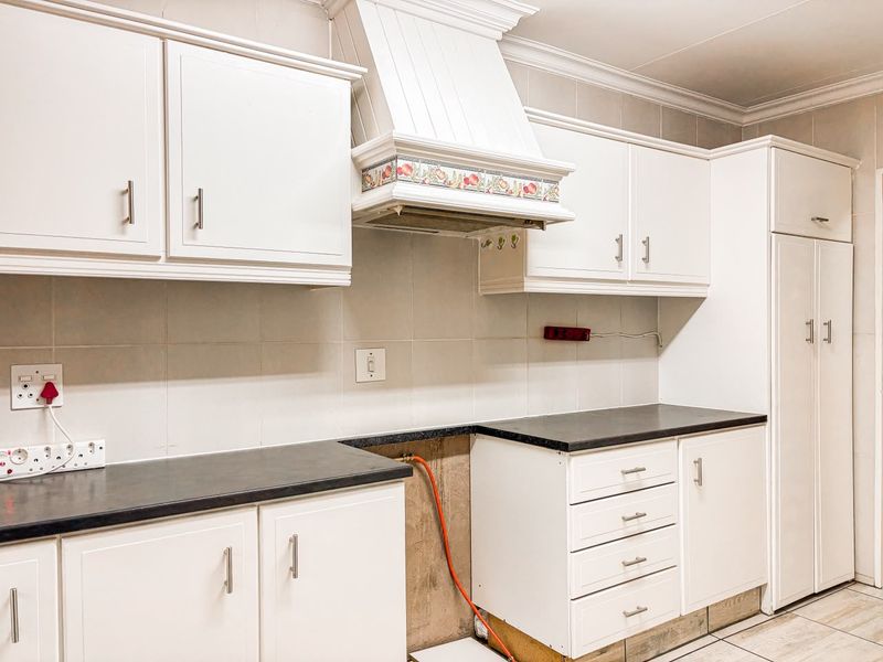 A kitchen featuring white cabinetry, tiled backsplash, and dark countertops, currently missing a stove unit with exposed gas piping.