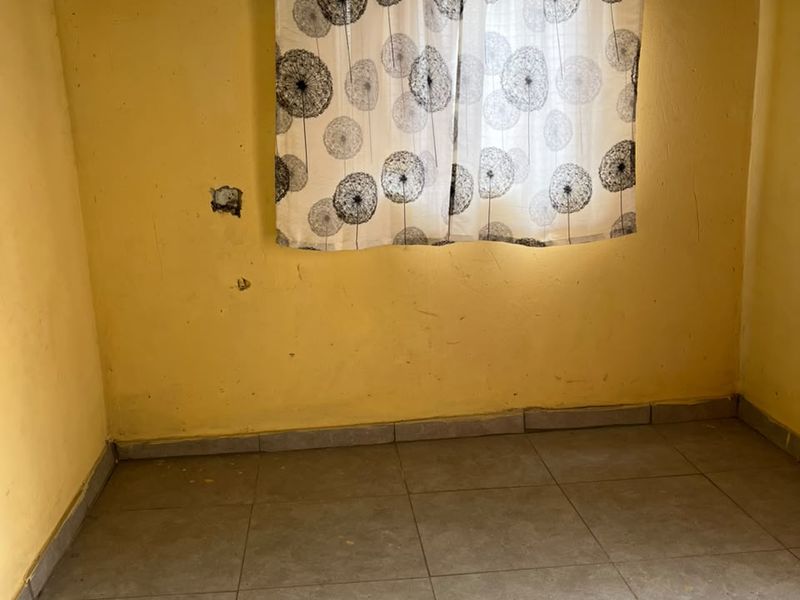 An empty bedroom featuring tiled flooring and yellow painted walls, requiring cosmetic updates and wall repairs.
