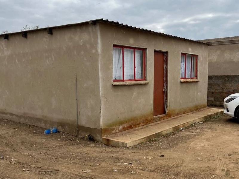 A modest single-story dwelling featuring a corrugated metal roof, red metal window frames, and an unfinished exterior wall finish.