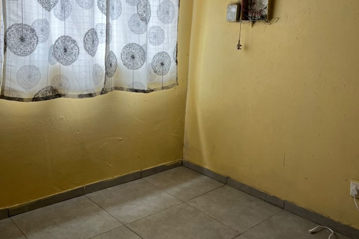 A small, empty bedroom featuring tiled flooring and an exposed electrical distribution board, requiring significant cosmetic repairs and electrical safety maintenance.