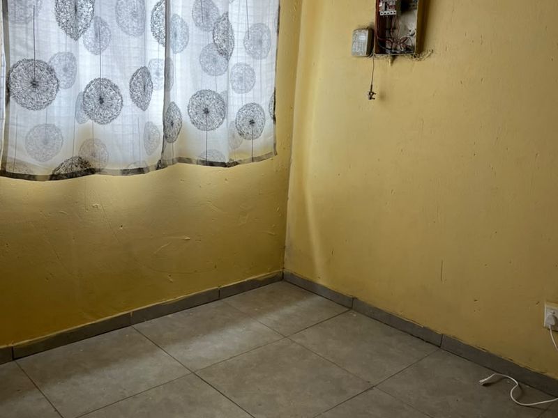 A small, empty bedroom featuring tiled flooring and an exposed electrical distribution board, requiring significant cosmetic repairs and electrical safety maintenance.
