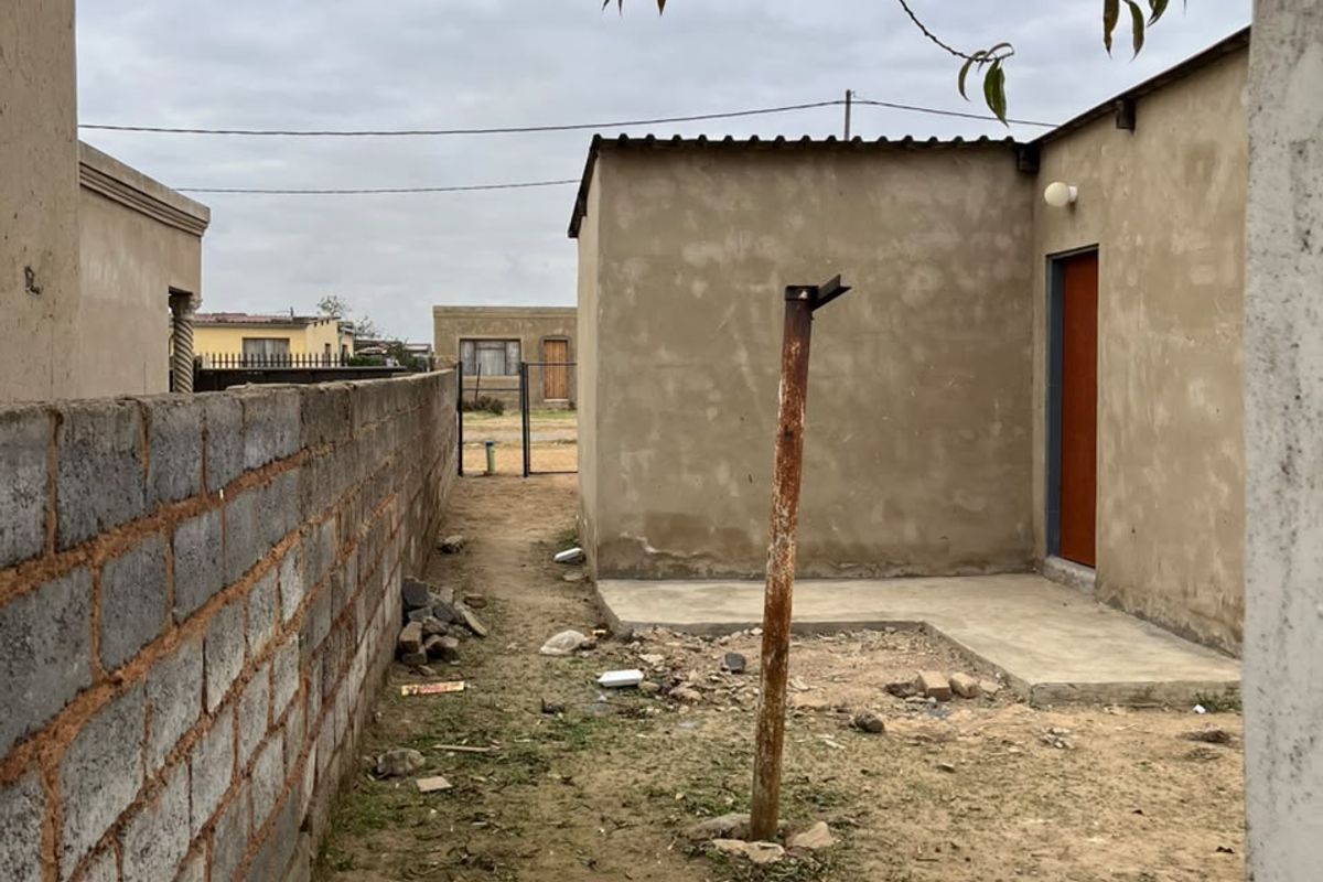 Rear exterior area featuring a concrete boundary wall, a small concrete slab, and an unfinished exterior wall with a single door entrance.