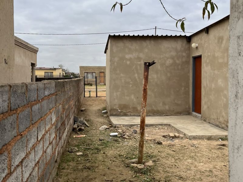 Rear exterior area featuring a concrete boundary wall, a small concrete slab, and an unfinished exterior wall with a single door entrance.
